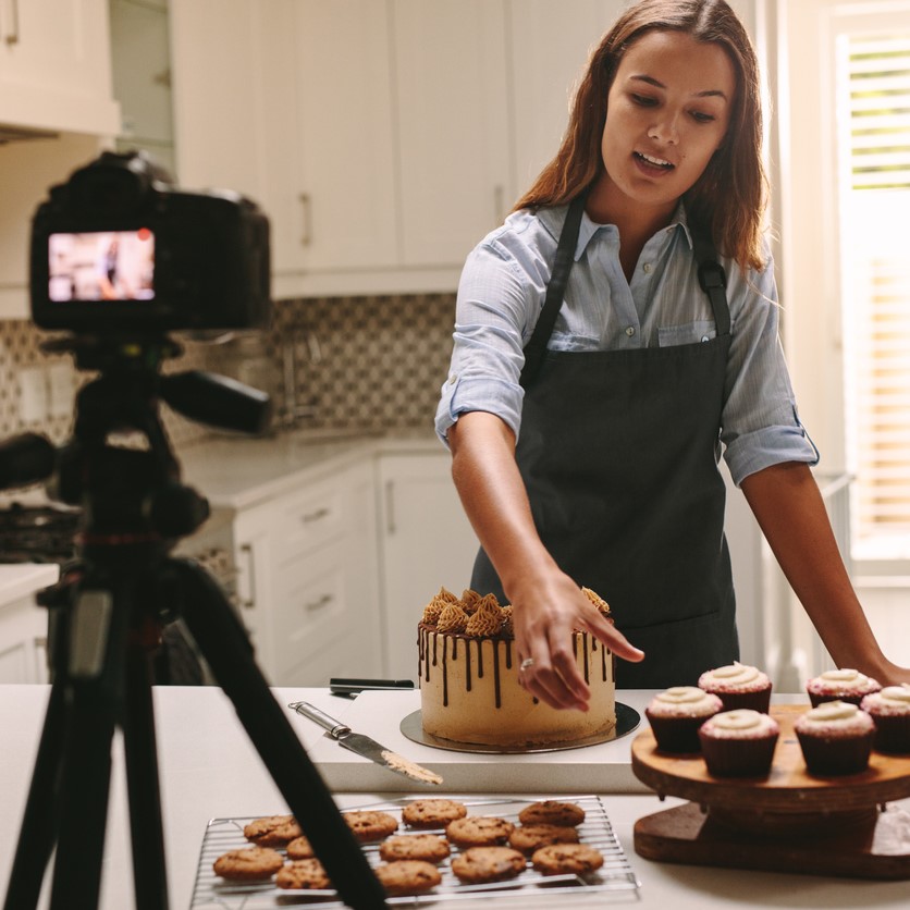 Retail Website Lifestyle Content -  Social media influencer woman recording video content in kitchen, showing confectionery on table. Female confectioner filming herself of her online culinary show.